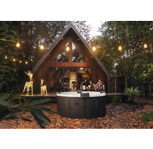 Kulatá venkovní vířivka v zahradě s moderním domem ve tvaru A, světelnými řetězy a osvětlenými dekoracemi sobů večer.