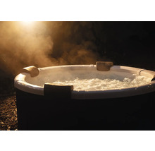 Kulatá nafukovací vířivka s bublající vodou, opěrkami hlavy a stoupající párou venku v noci.