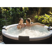 Pár relaxuje ve vířivce s bublinkami na zahradě, obklopený zelenými rostlinami a stromy.