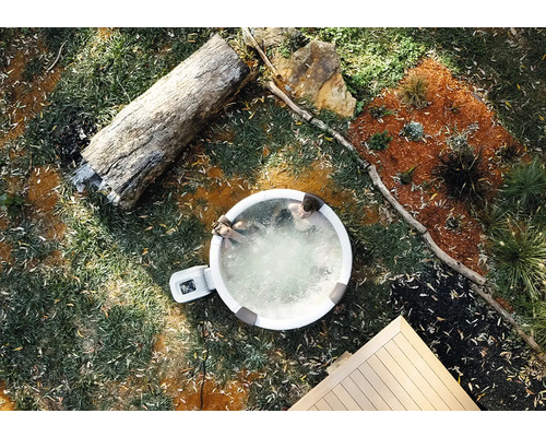 Nafukovací vířivka na zahradě z ptačí perspektivy se dvěma osobami, kmenem stromu a dřevěnou terasou.