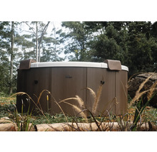 Kulatá vířivka MSpa s venkovním obložením v dekoru dřeva a dvěma opěrkami hlavy v zahradě.