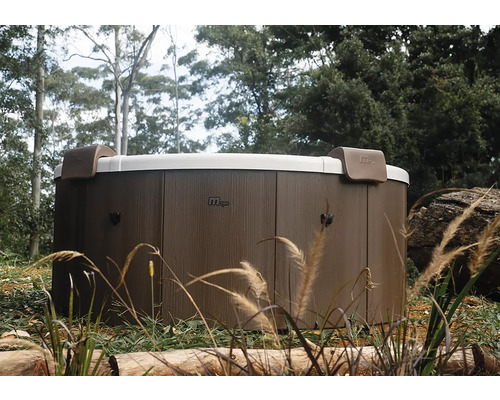 Kulatá vířivka MSpa s venkovním obložením v dekoru dřeva a dvěma opěrkami hlavy v zahradě.