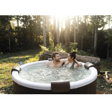 Pár relaxuje v kulaté venkovní vířivce v zahradě se stromy. Vířivka má opěrky hlavy a bublající vodu.