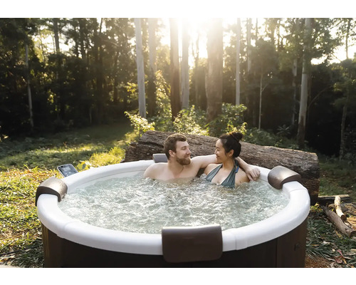 Pár relaxuje v kulaté venkovní vířivce v zahradě se stromy. Vířivka má opěrky hlavy a bublající vodu.