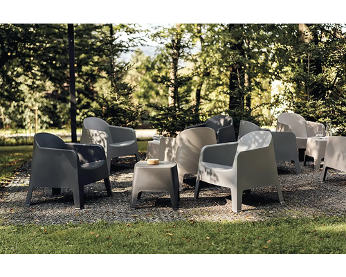 Moderní zahradní křesla a odkládací stolky z plastu v zastíněné zahradě na štěrku.