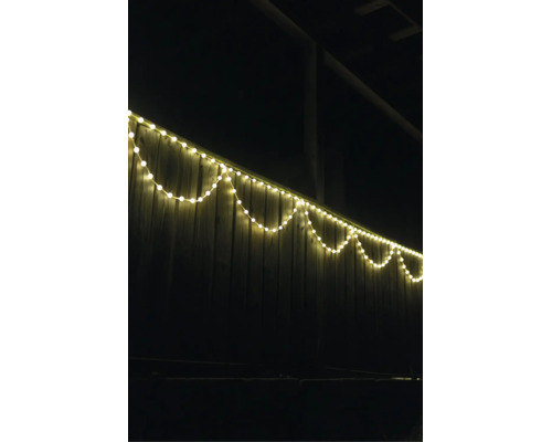 LED světelný řetěz teple bílá na dřevěném plotě v exteriéru v noci.