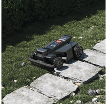 Robotická sekačka Segway Navimow přejíždí kamenné nášlapy v zahradě s trávníkem.