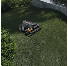 Robotická sekačka na zeleném trávníku v zahradě se sklonem a keři.