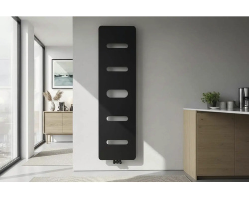 Moderní vertikální designový radiátor v černé barvě s horizontálními otvory na bílé stěně ve světlé minimalistické místnosti.