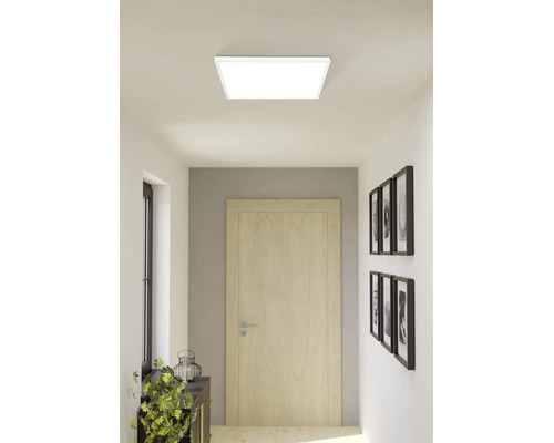 Čtvercový LED stropní panel ve světlé moderní chodbě s dřevěnými dveřmi a dekoracemi na stěně.