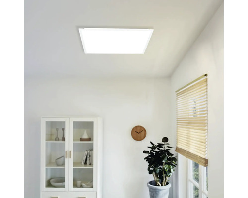 Čtvercový LED panel na stropě v jasně, moderně zařízeném pokoji s vitrínou, nástěnnými hodinami a rostlinou.