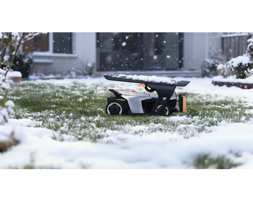 Robotická sekačka v garáži na zasněženém trávníku během sněžení před domem.
