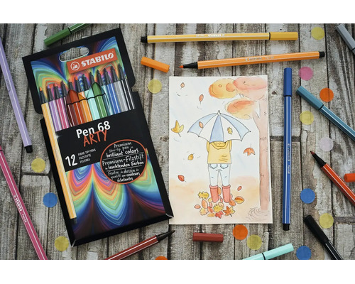 Sada 12 fixů STABILO Pen 68 Arty s podzimní kresbou a rozházenými pery na dřevěném podkladu.
