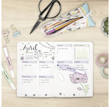 Pohled shora na světlý, uspořádaný pracovní stůl s otevřeným bullet journalem, zvýrazňovači Stabilo Swing Cool, nůžkami a papírenským zbožím.