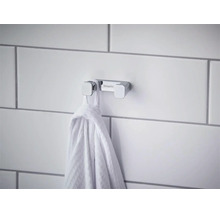 Dvojitý háček na ručníky Hansgrohe z chromu na dlážděné stěně s pověšeným ručníkem.