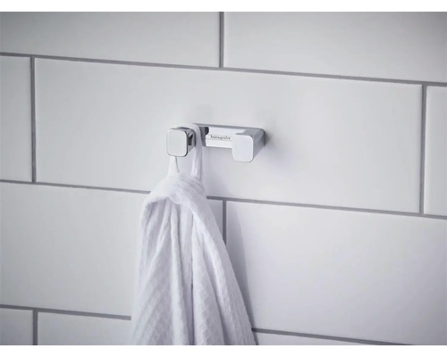 Dvojitý háček na ručníky Hansgrohe z chromu na dlážděné stěně s pověšeným ručníkem.