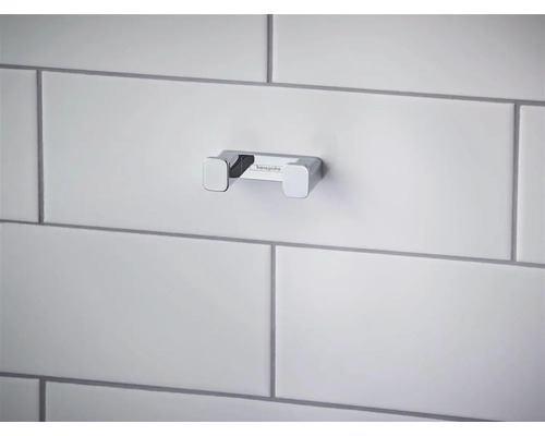 Dvojitý koupelnový háček Hansgrohe z chromovaného kovu, namontovaný na dlážděné stěně.