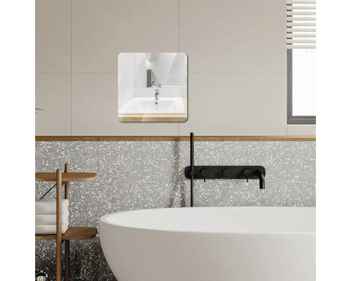 Moderní koupelna se čtvercovým zrcadlem se zaoblenými rohy, bílou vanou, černými bateriemi a stěnami v designu terrazzo.