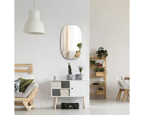 Oválné nástěnné zrcadlo ve světlém obývacím pokoji nad komodou s rostlinami a minimalistickým dekorem.