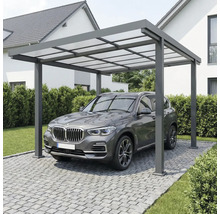 Moderní hliníkový přístřešek pro auto s průsvitnou střechou nad vozidlem na dlážděné příjezdové cestě u domu.