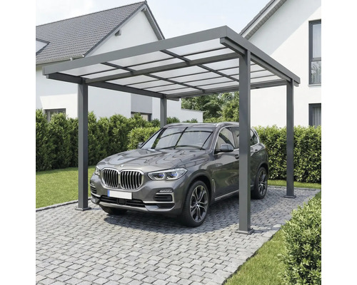 Moderní hliníkový přístřešek pro auto s průsvitnou střechou nad vozidlem na dlážděné příjezdové cestě u domu.