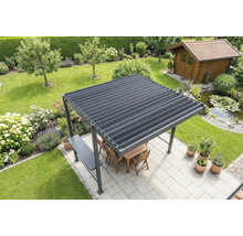 Volně stojící pergola s lamelovou střechou na světlé terase v zahradě, včetně dřevěného nábytku, přilehlého jezírka a zahradního domku v pozadí.