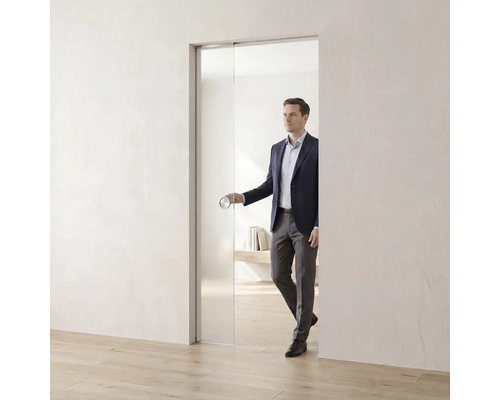 Skleněné posuvné dveře ve světlé, minimalistické místnosti s osobou používající kulatou dveřní kliku.