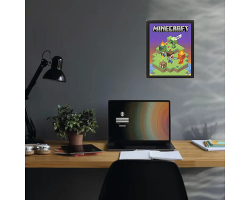 Plakát Minecraft v černém rámu na tmavé stěně nad psacím stolem s notebookem a rostlinou.