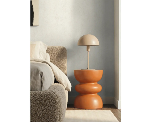 Stolní lampa ve tvaru houby na moderním sochařském odkládacím stolku vedle postele s texturovaným čelem.