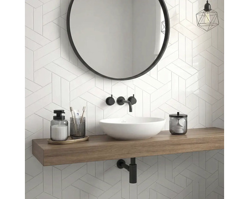 Moderní koupelna s bílým umyvadlem na dřevěné desce, kulatým zrcadlem, černou baterií a geometrickým obkladem.