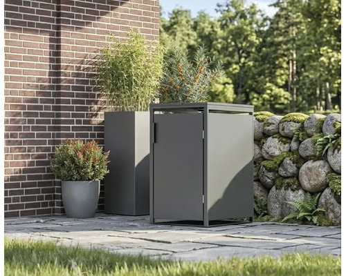 Moderní kovový box na popelnice a odpovídající květináč na dlážděné terase vedle cihlové zdi a zdi z přírodního kamene.