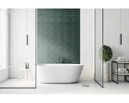 Moderní koupelna s volně stojící vanou před tmavě zelenou obloženou stěnou, minimalistický design se skleněnými prvky.