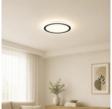 Moderní kulaté stropní LED svítidlo s černým okrajem v světlém, minimalistickém obývacím pokoji s bílými stěnami a světlým nábytkem.