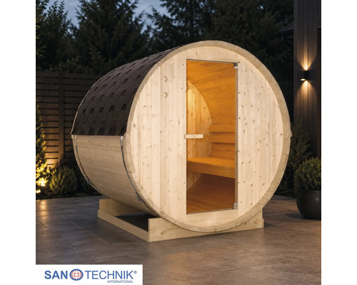 Sudová sauna Sanotechnik ze dřeva na terase za soumraku s prosklenými dveřmi, vnitřním osvětlením a šindeli. Sanotechnik Logo.