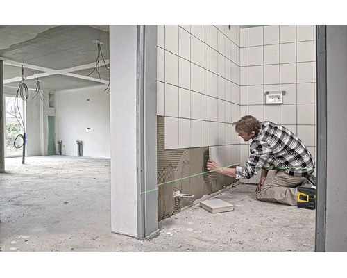 Řemeslník pokládá bílé obklady pomocí lepidla na dlaždice a křížového laseru na staveništi.