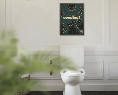Rámovaný obraz na stěnu s černými kočkami a textem are you pooping? nad bílou toaletou v koupelně.