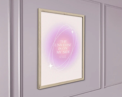 Rámovaný obraz na stěnu s nápisem THE UNIVERSE IS ON MY SIDE na abstraktním pozadí, ve světlém dřevěném rámu na zdi.