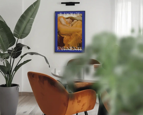 Moderní interiér se zarámovaným plakátem s textem Il Dolce Far Niente na stěně, velkou rostlinou, sametovým křeslem a stolem.