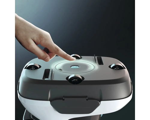 Prst mačká osvětlené tlačítko napájení na horní straně bazénového čisticího robotu se čtyřmi malými kolečky.