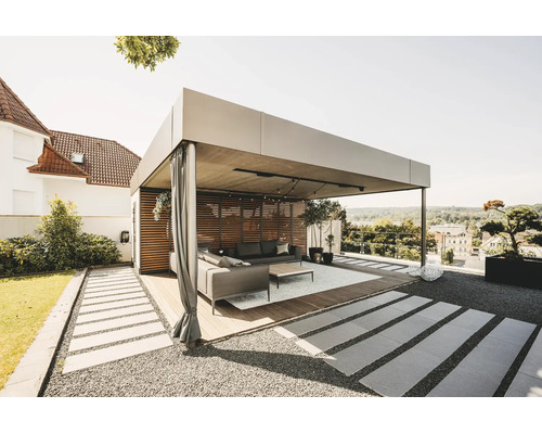 Moderní, světlá kovová pergola s dřevěnou lamelovou stěnou, závěsy a lounge nábytkem na dřevěné terase v zahradě.