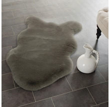 Měkká imitace ovčí kůže ve tvaru zvířete na dlaždicové podlaze vedle keramického džbánu.