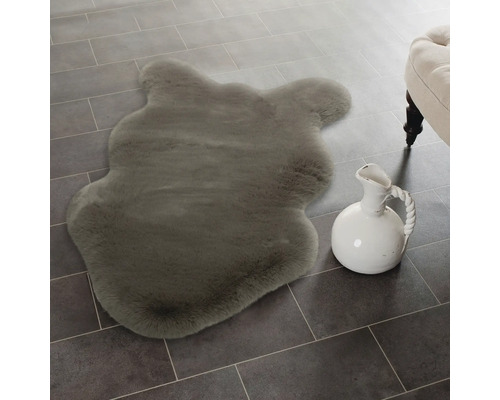 Měkká imitace ovčí kůže ve tvaru zvířete na dlaždicové podlaze vedle keramického džbánu.