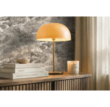 Moderní stolní lampa s kulatým stínidlem na dřevěné komodě před lesní tapetou, doplněná knihami a vonnou svíčkou. Světlé a uspořádané.