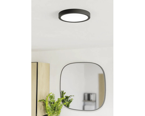 Moderní kulaté stropní LED svítidlo v černé barvě ve světlé místnosti nad zrcadlem a rostlinou.
