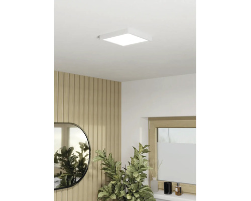 Čtvercový LED panel jako stropní svítidlo v moderně zařízeném pokoji s dřevěným lamelovým obkladem, zrcadlem a pokojovou rostlinou.