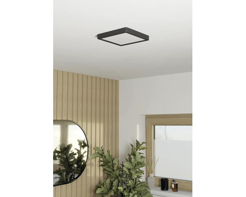 Čtvercové stropní LED svítidlo v osvětlené, moderně zařízené místnosti s nástěnnými panely v dekoru dřeva, oválným zrcadlem a pokojovou rostlinou.
