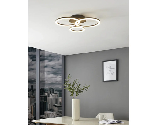 Moderní LED stropní svítidlo se čtyřmi světelnými kruhy v jasné místnosti se šedou stěnou, výhledem na město a bílým stolem.