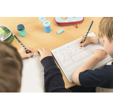 Děti píší u stolu ergonomickými tužkami na pracovní list a do sešitu, včetně ořezávátek a penálů.
