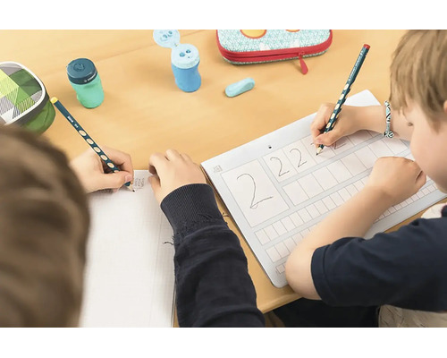 Děti píší u stolu ergonomickými tužkami na pracovní list a do sešitu, včetně ořezávátek a penálů.