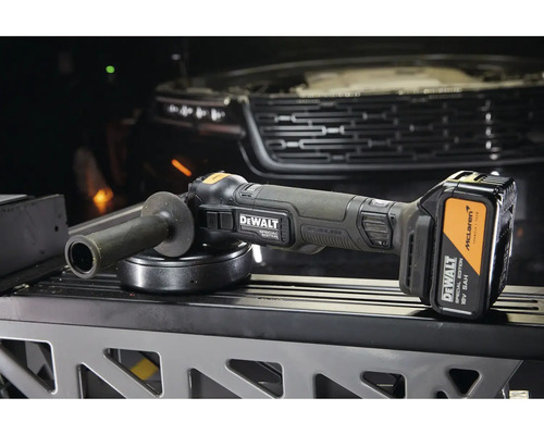 Akumulátorová úhlová bruska DeWalt Special Edition 18 V s akumulátorem a rukojetí před vozidlem.